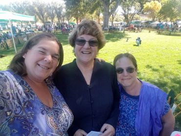 Three women smiling at an outdoor event on a sunny day.
