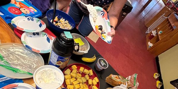 Person serving food onto a paper plate at a table with various dishes.