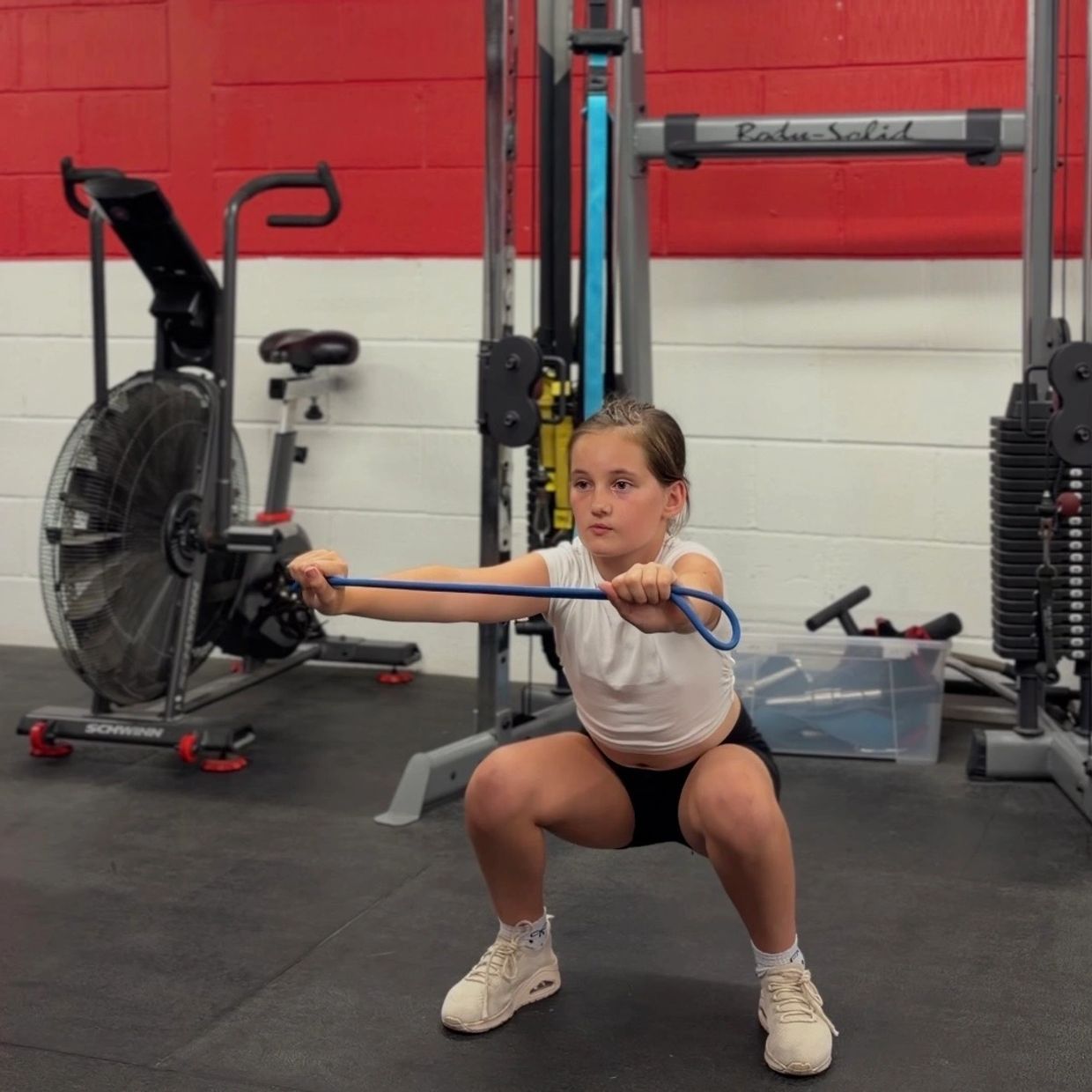 Young girl doing resistance band squats in a gym.