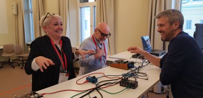 Three people laughing and enjoying a moment around a table with electronic devices.