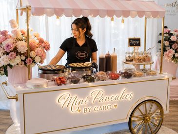 Elegant mini pancake cart with toppings and a server.