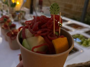 A cup filled with fruit and spicy mango strips, decorated with a small leaf pick.