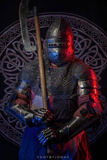 Armored knight with a battle axe and chainmail in front of a Celtic design.