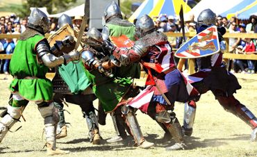 Medieval knights in armor engage in a lively battle reenactment.