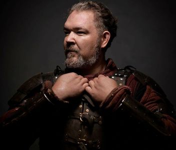 Man in medieval armor adjusting his collar, looking determined.