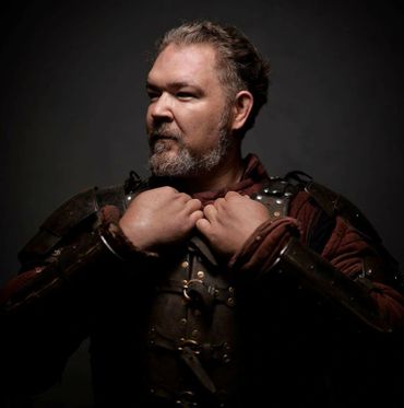 Man in medieval armor adjusting his collar, looking determined.