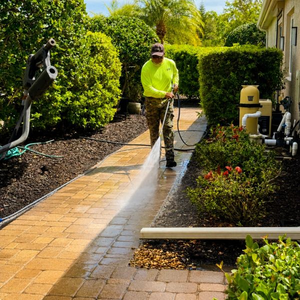 Person pressure washing a brick pathway on a sunny day.