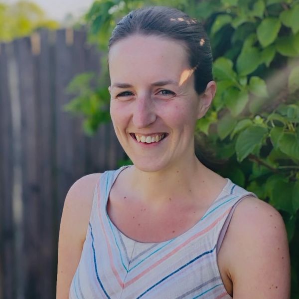 Smiling woman outdoors with greenery in the background.