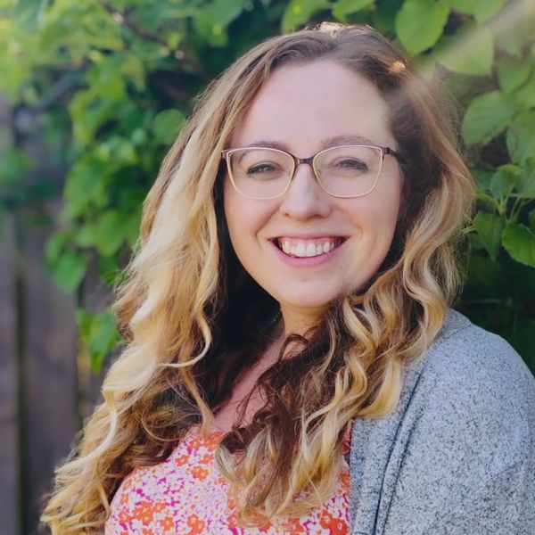 Smiling woman with glasses and wavy hair outdoors.