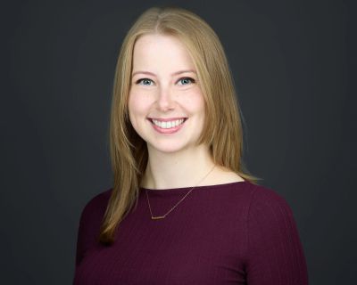 Smiling woman with blonde hair in a maroon top against a dark background.