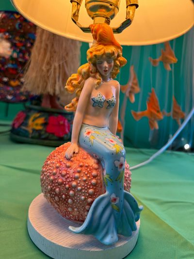 A lamp featuring a mermaid figurine sitting on a textured coral base.