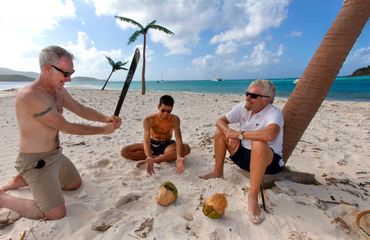 Tennis start John McEnroe takes a hack on a coconut while tennis champ Novac Djokovich and Sir Richa