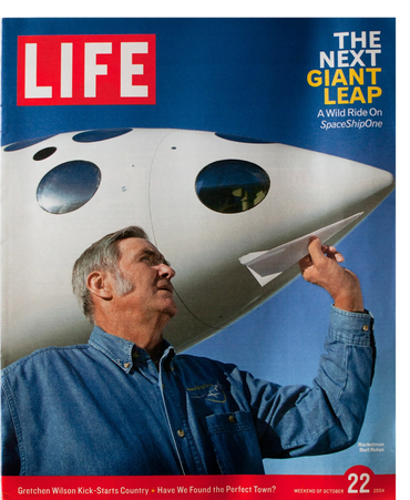 Designer Burt Rutan holds a paper airplane in front of WhiteKnight 2 at Mojave Air and Spaceport