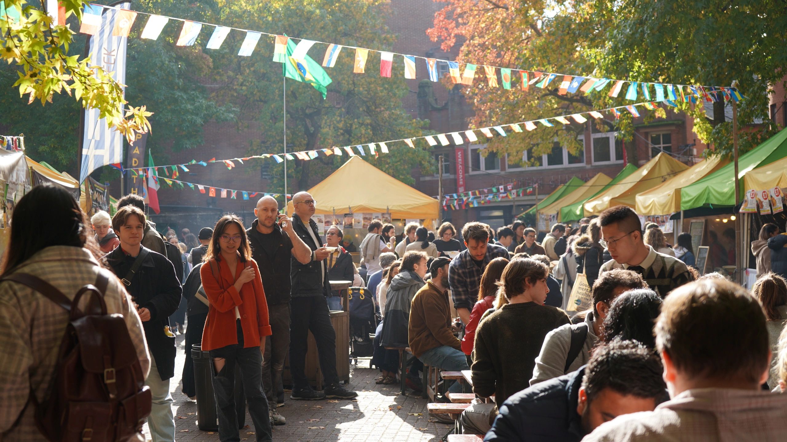 Crowded outdoor market with colorful flags and people enjoying the day.