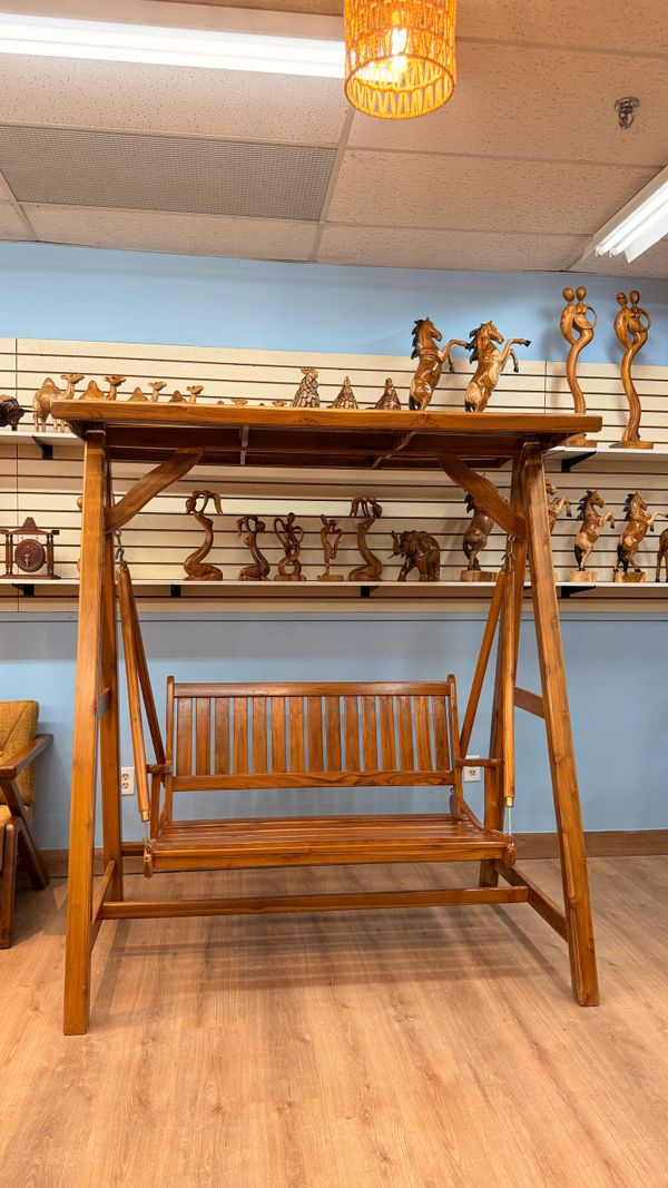 Wooden swing chair with a canopy in a room with wooden sculptures.
