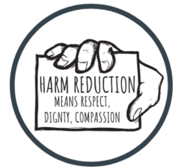 Hand holding a sign about harm reduction and compassion.