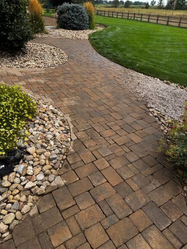 Curved brick pathway bordered by rocks and greenery in a well-maintained garden.
