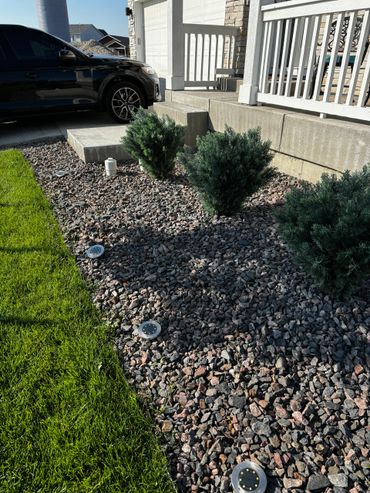 Rock garden with small shrubs and solar lights beside a house porch.