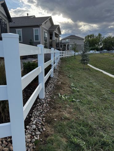 White fence runs alongside suburban homes under a cloudy sky.
