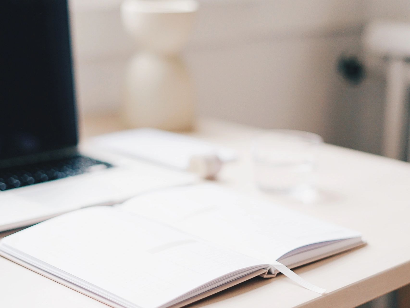 Open book, glass of water and laptop on a desk.
