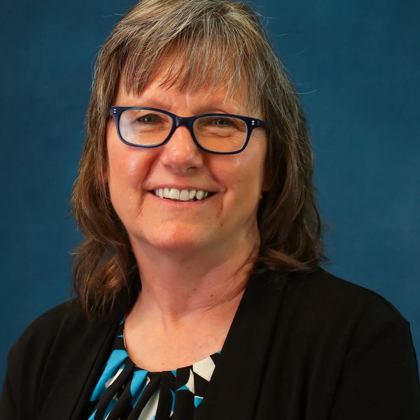Smiling woman with glasses against blue background.