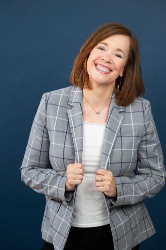 Smiling woman in a gray plaid blazer against a blue background.