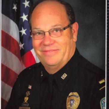 Portrait of a male police officer in uniform with an American flag in the background.