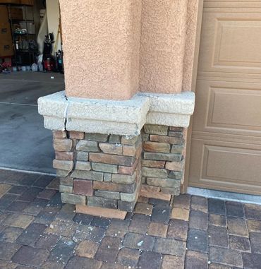 Damaged stone column at the base of a house's stucco pillar, with cracks and missing pieces near the garage.