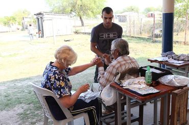 A man helps an elderly couple with their hands in an outdoor setting.