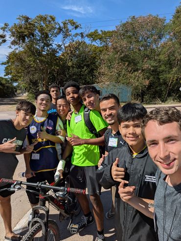 A group of young men smiling outdoors with a bicycle under a clear blue sky.