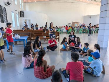 Children and adults engaged in group activities inside a spacious hall.