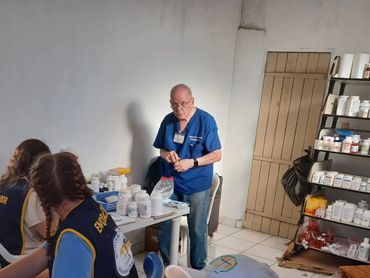 A healthcare professional in blue scrubs with two women in vests at a table with medicine bottles.