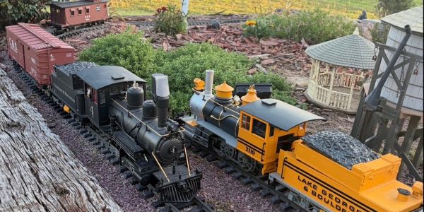 Two detailed model trains on garden tracks with miniature scenery.