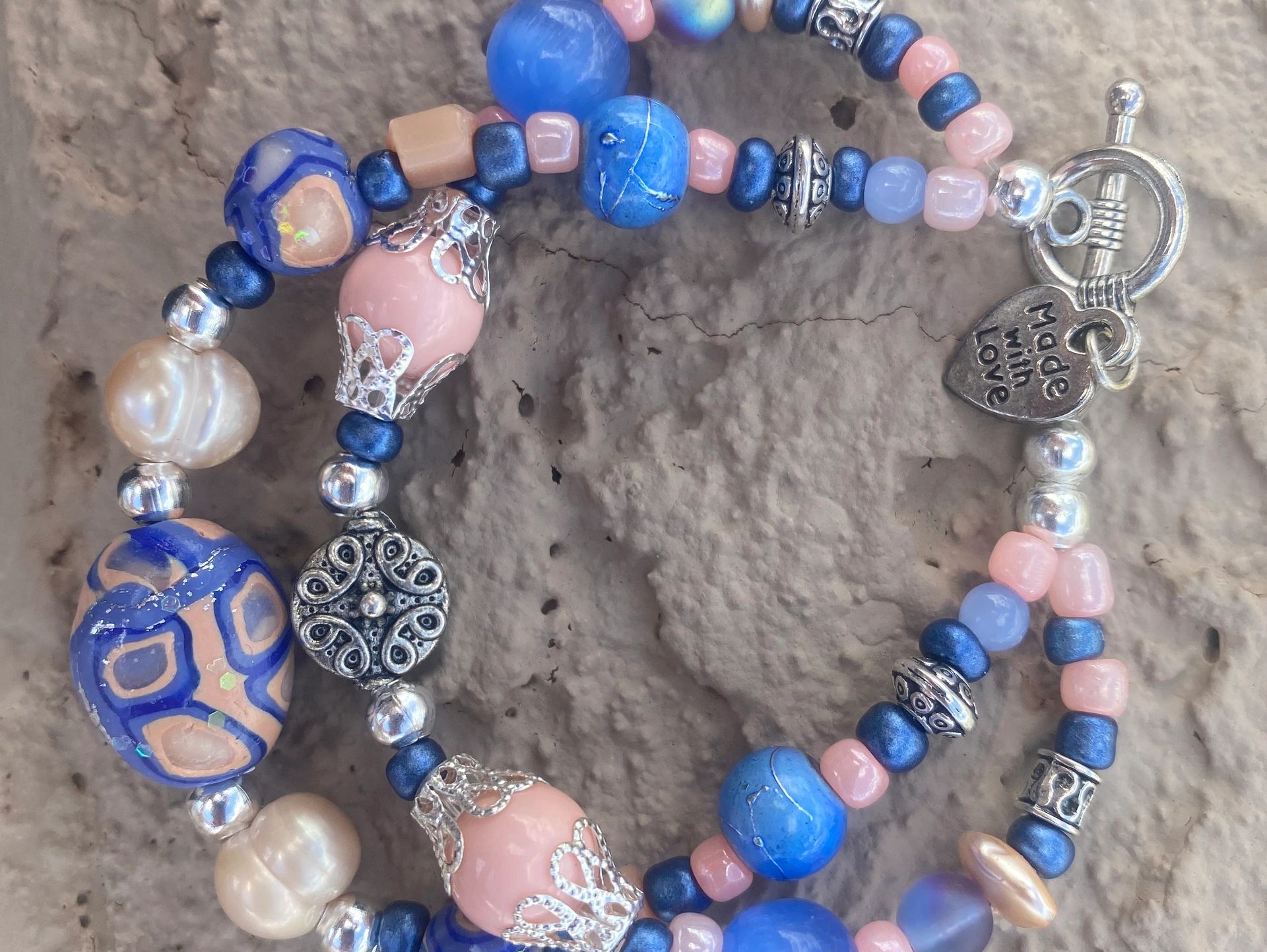 This bracelet is created with handmade clay beads of periwinkle blue and peach and a charm