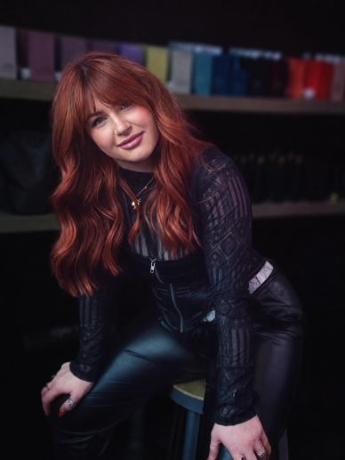 Woman with red hair poses confidently indoors.