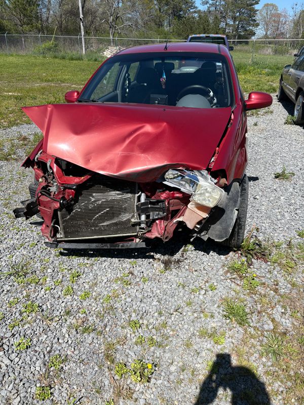 Red car with severe front-end damage parked on gravel.
