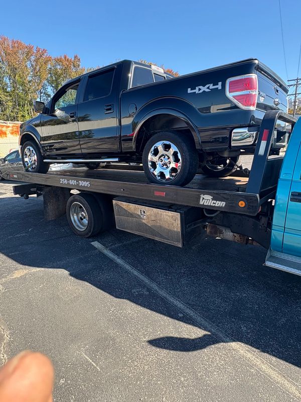 Black 4x4 pickup truck on a tow truck bed in a parking lot.
