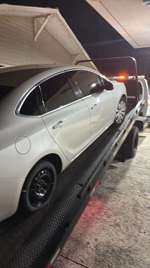 A white car being towed on a flatbed truck at night.