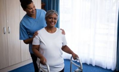 Nurse assisting an elderly woman using a walker indoors.