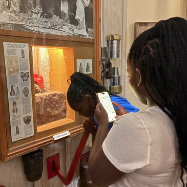 Woman taking photo of another woman examining exhibit.