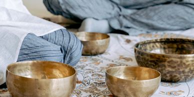 Person sitting cross-legged near a set of brass singing bowls on patterned cloth.