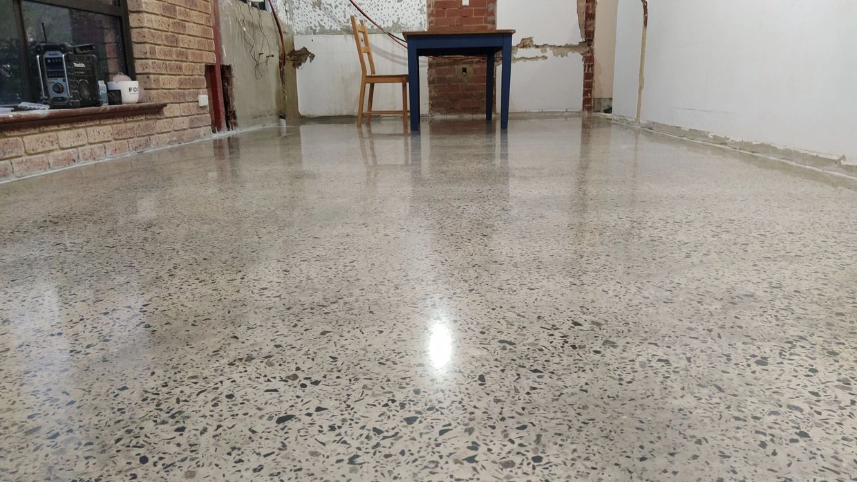 Polished terrazzo floor with a single chair and table in an unfinished room.
