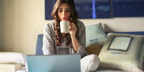 A woman comleting an online course on her bed using her laptop.