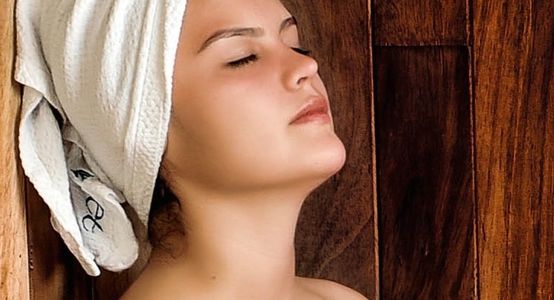woman in a sauna with a white towel on her head and body and eyes are closed