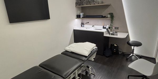 A modern treatment room with a black therapy table and white walls.