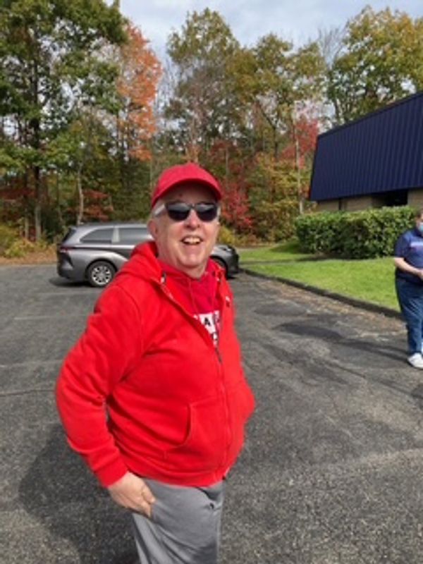 Man in red hoodie and cap smiling outdoors on a sunny day.