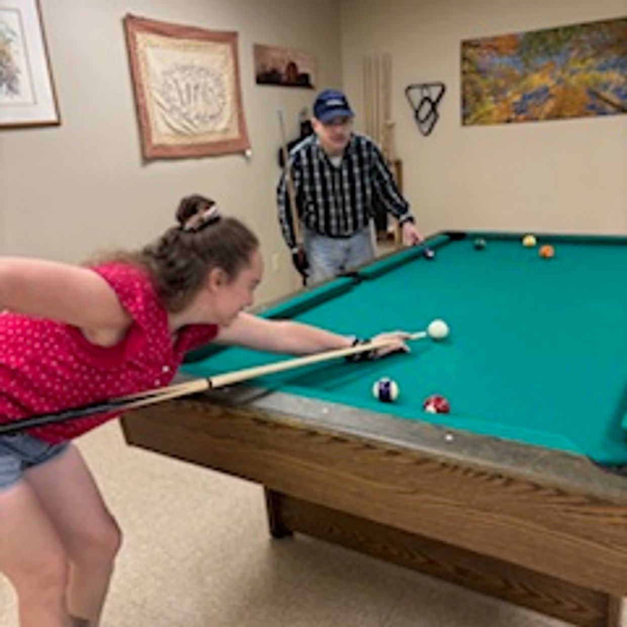 A young woman aiming to strike the cue ball on a pool table while a man watches.