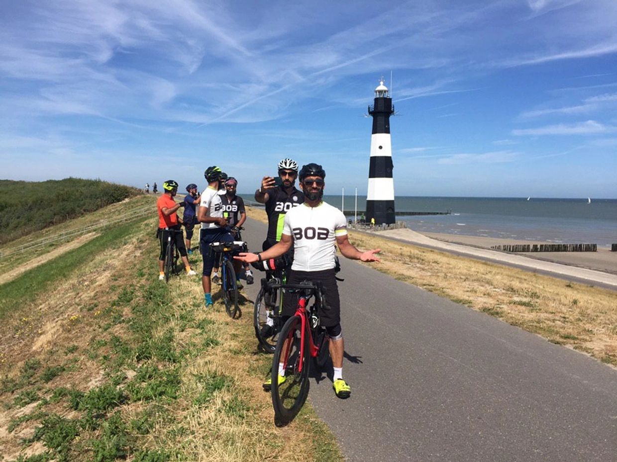 Cyclists posing near a black and white lighthouse by the sea.