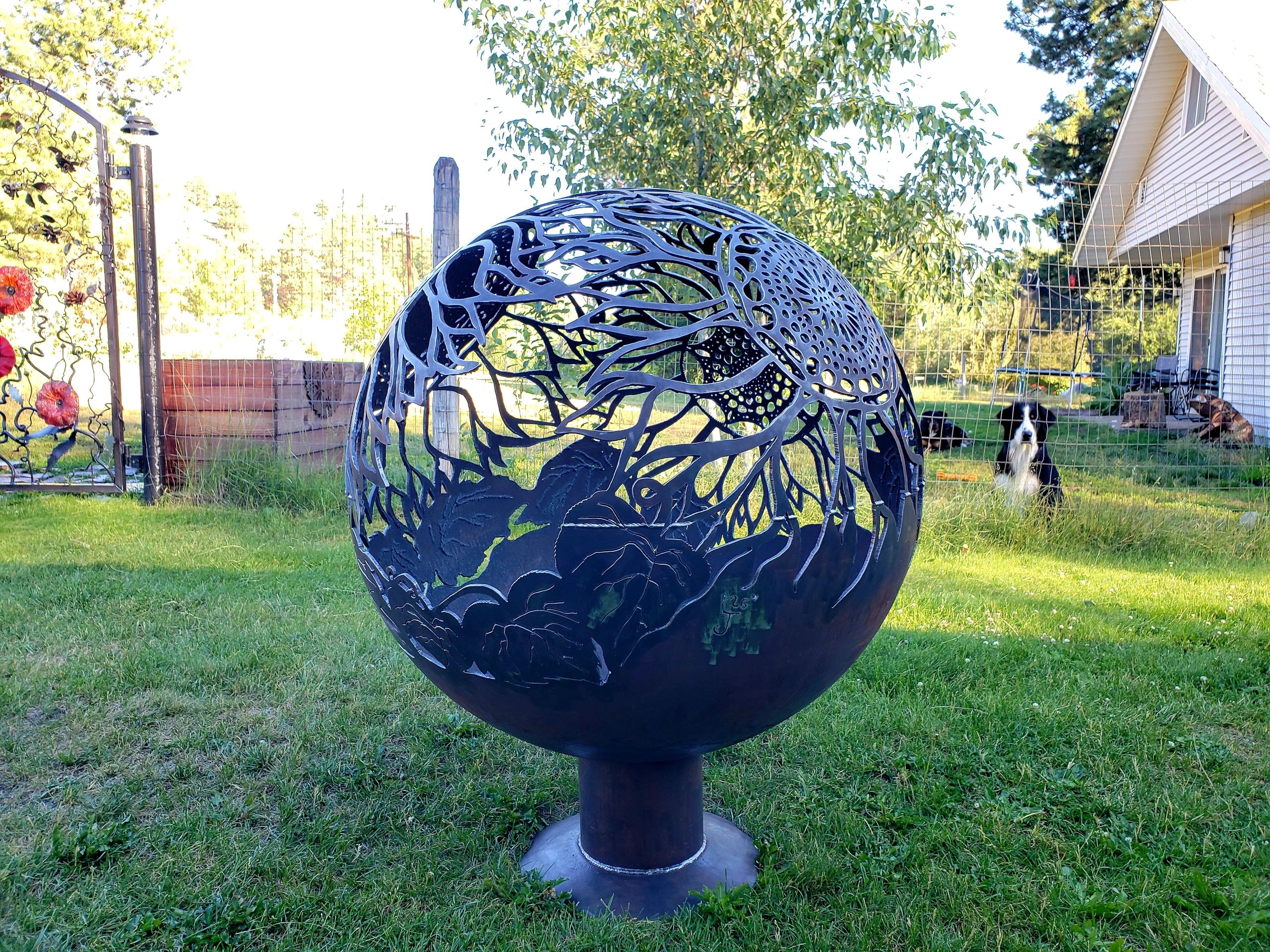Intricate metal fire pit sphere with floral designs in a backyard.