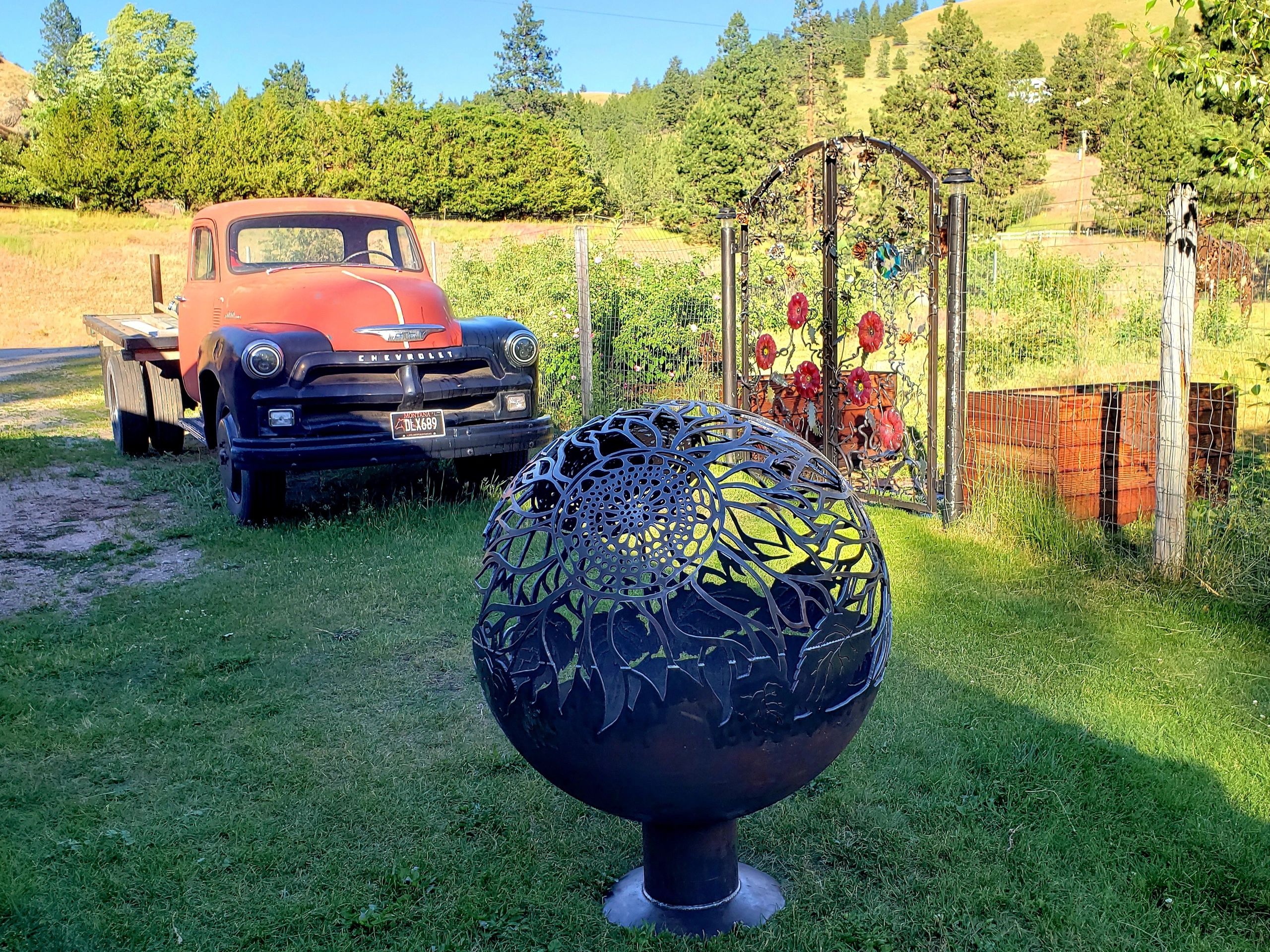 Vintage Chevrolet truck near ornamental garden gate and metal spherical sculpture.